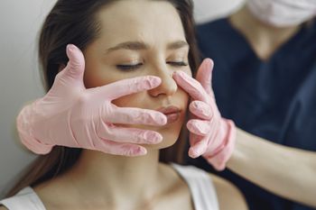 A woman is getting her face examined by a doctor wearing pink gloves.