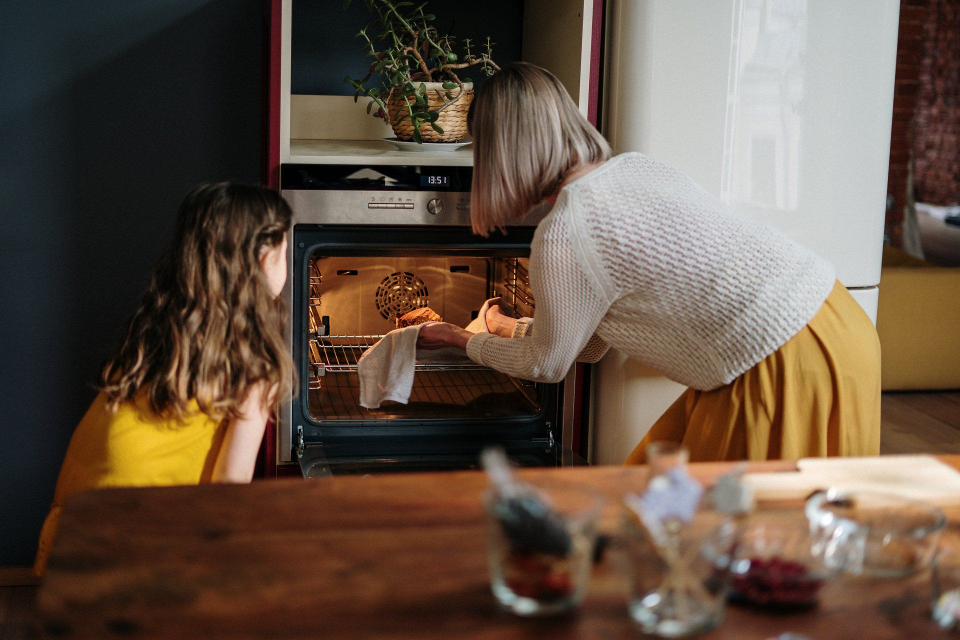 a woman and a little girl are looking into an oven .
