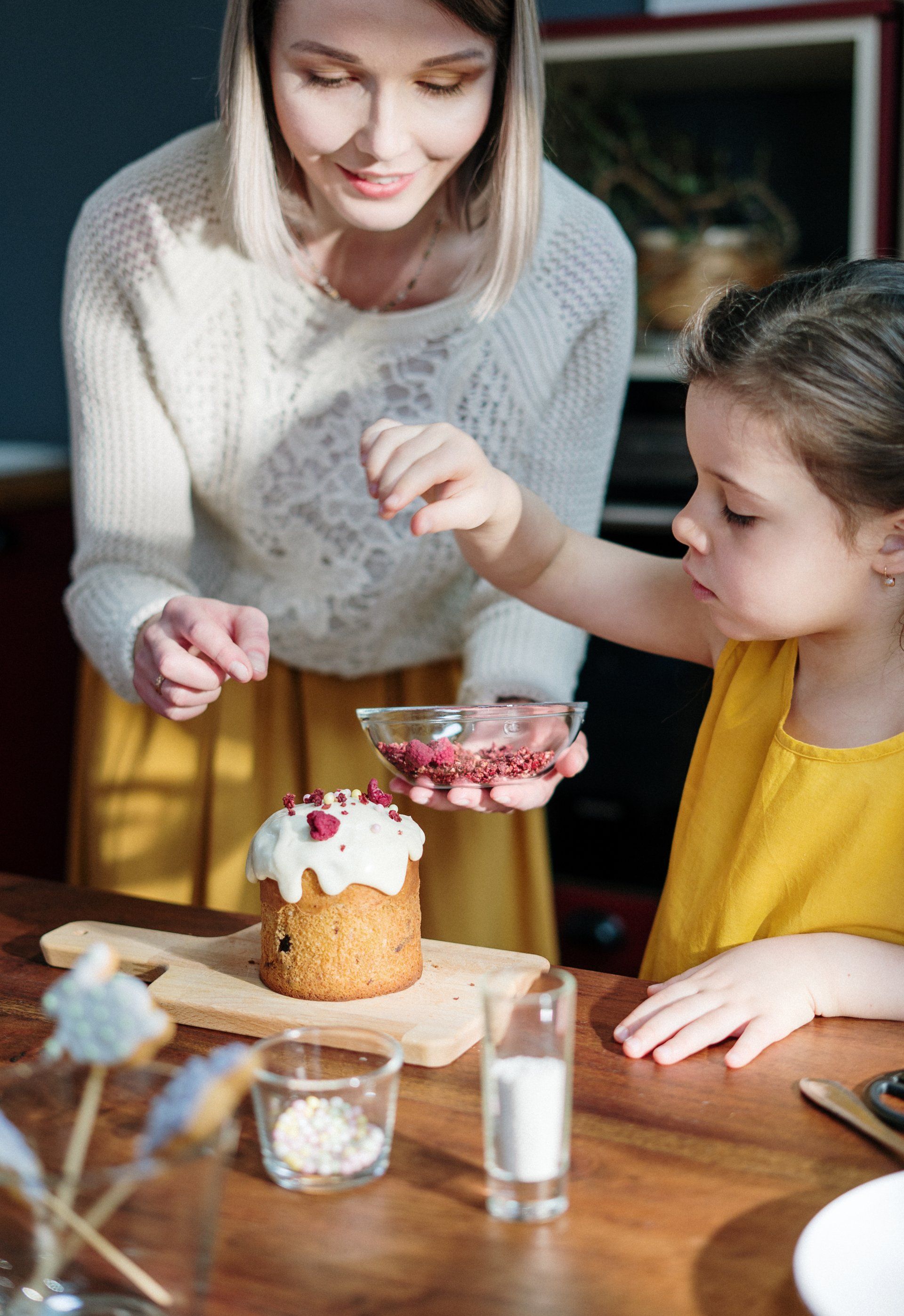 A woman and a little girl are sitting at a table decorating a cake.