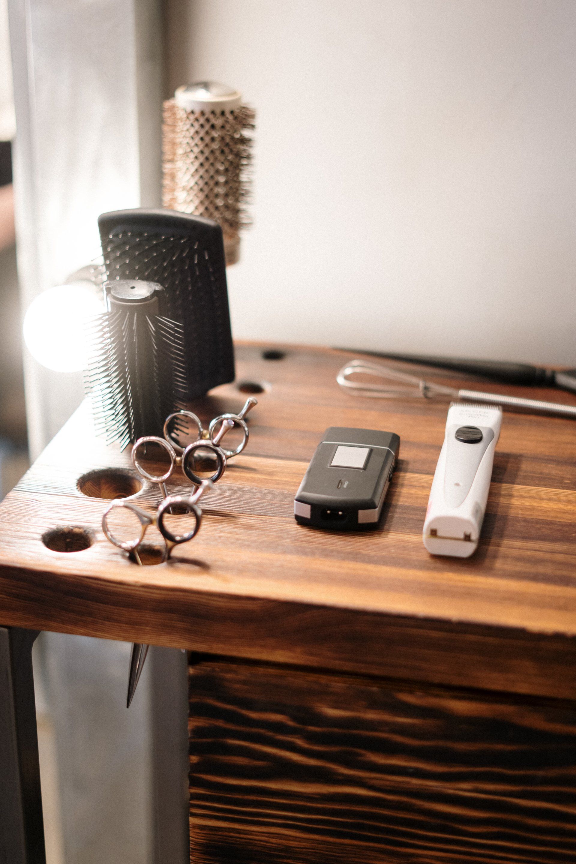 Haircutting tools on a wooden table: scissors, clippers, comb, and hairbrush.