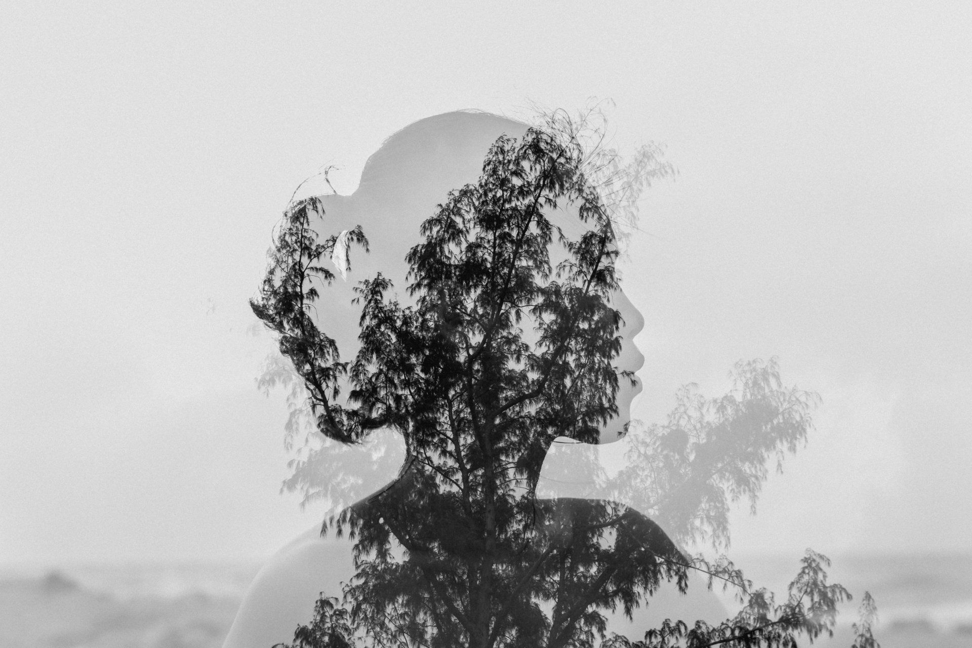 a black and white photo of a woman with trees in her hair .