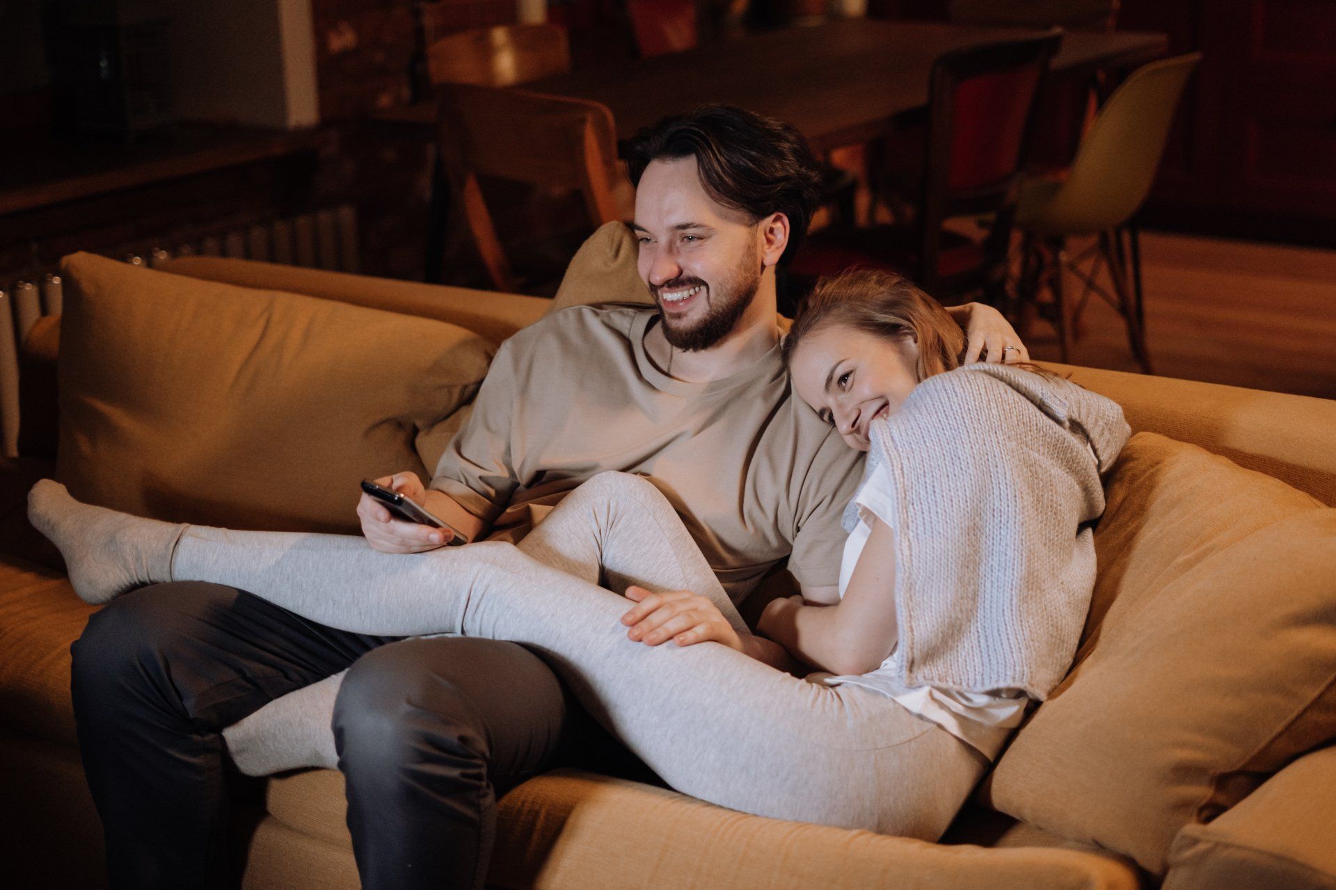 a man and a woman are sitting on a couch watching tv co-regulating after a successful premarital counseling session in Grapevine Texas