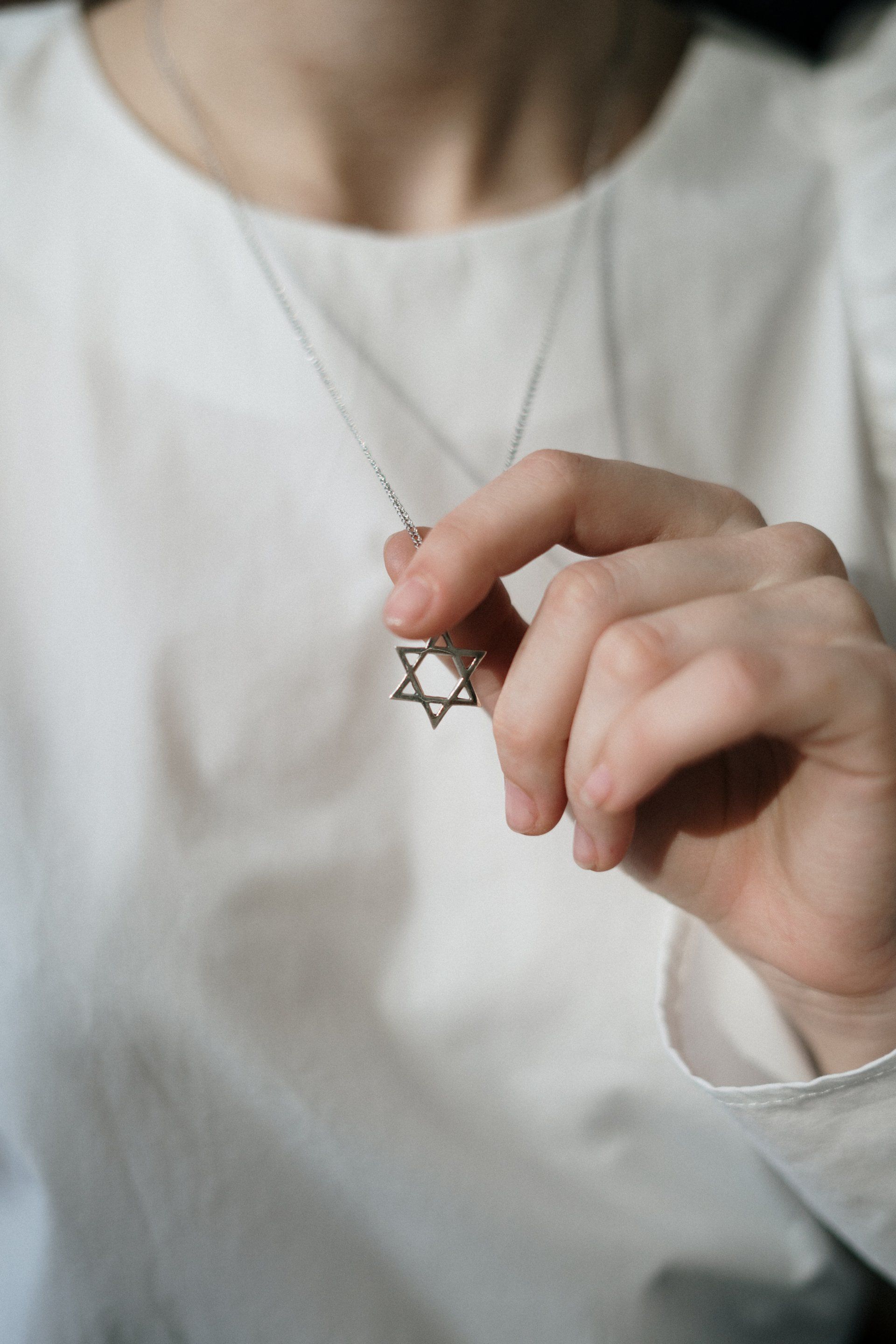 A woman is holding a necklace with a star of david pendant.
