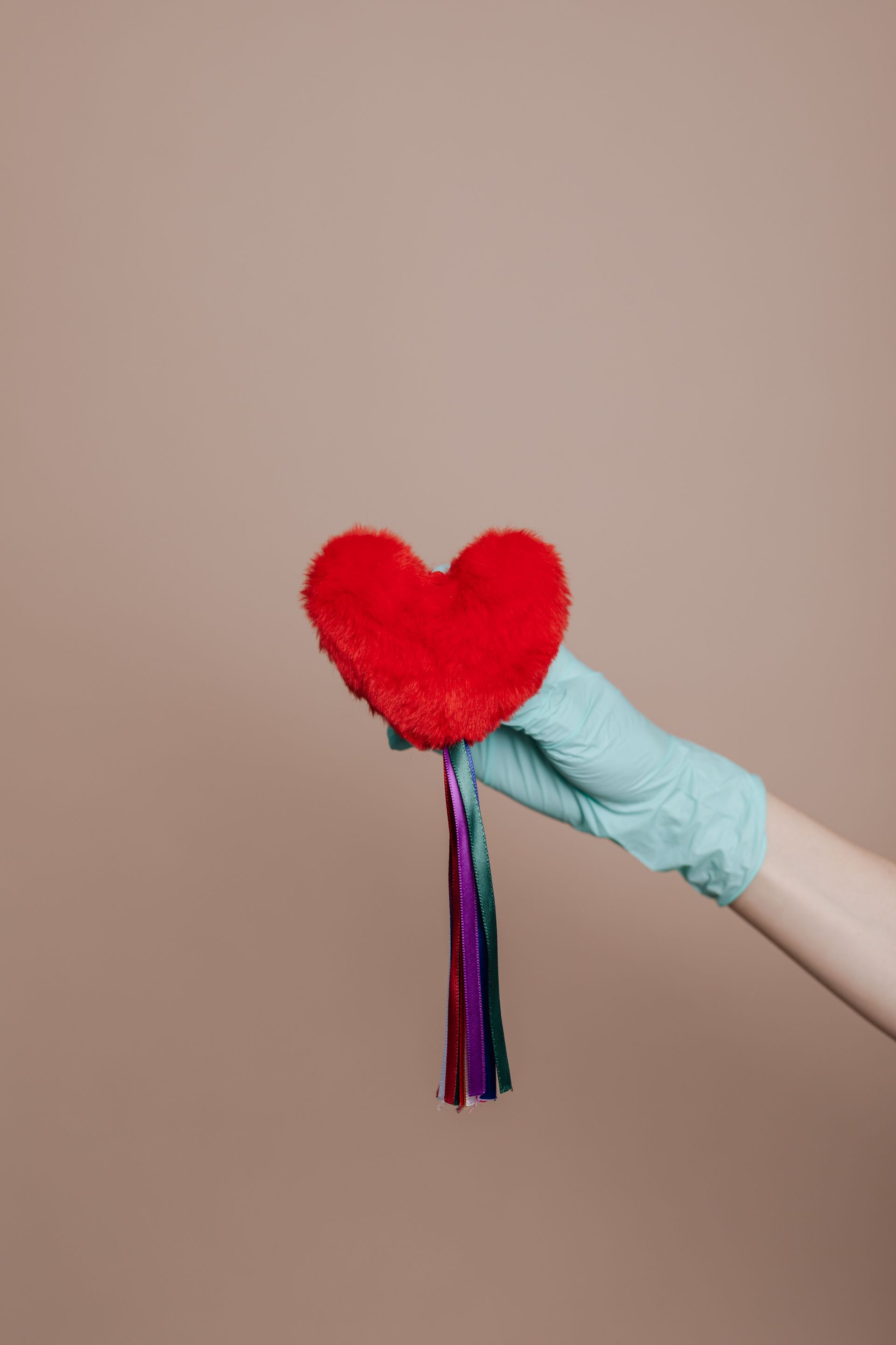 a person wearing a glove is holding a red heart with a tassel .