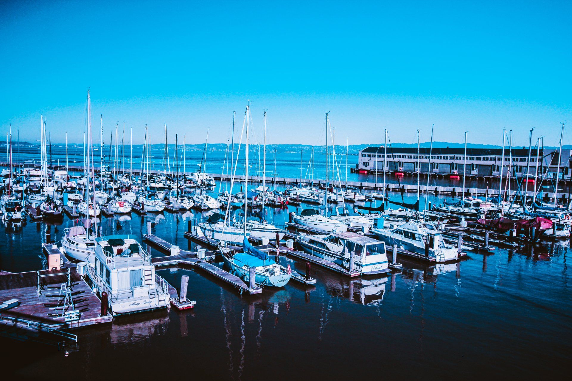 A row of boats are docked in a marina on a sunny day.