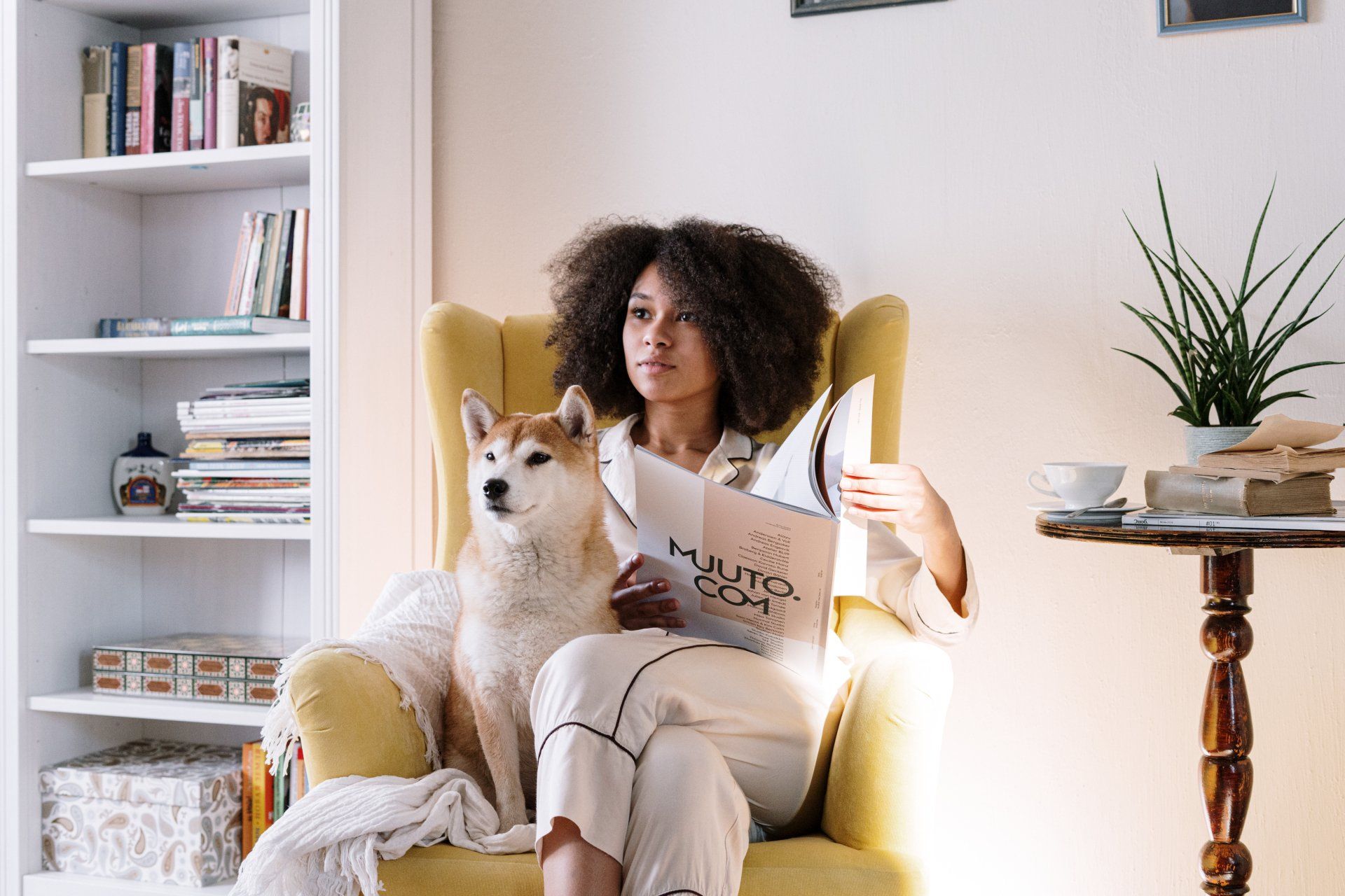Una donna è seduta su una poltrona con il suo cane e legge un libro.