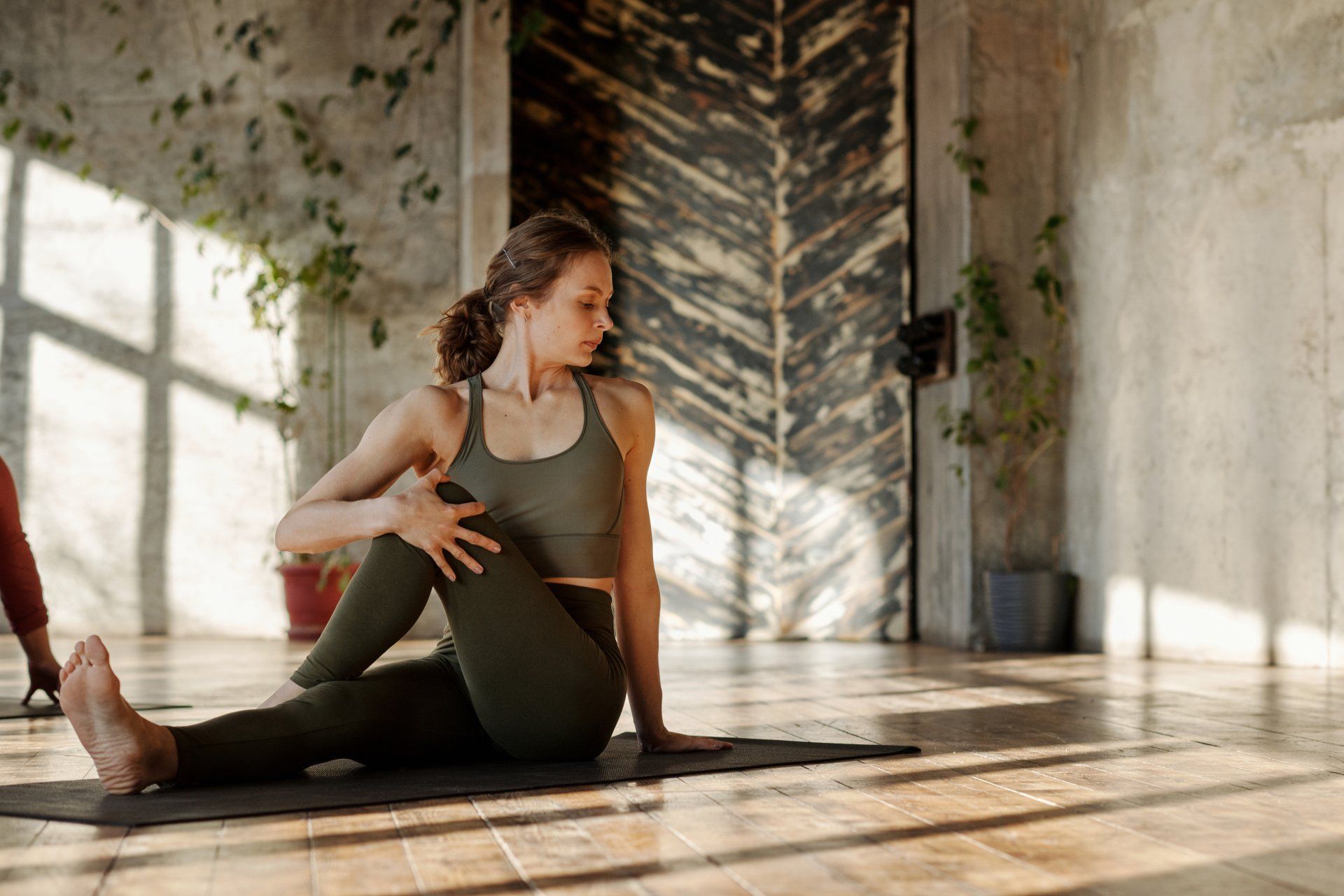 A woman is sitting on a yoga mat in a room.