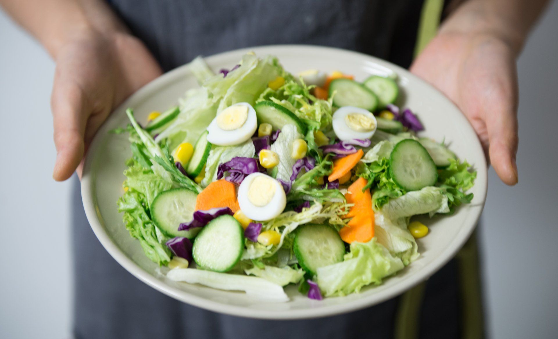 A person is holding a plate of salad in their hands.