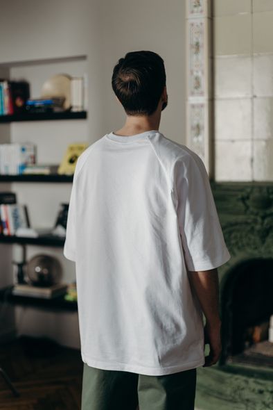 A man in a white t-shirt is standing in front of a fireplace in a living room.