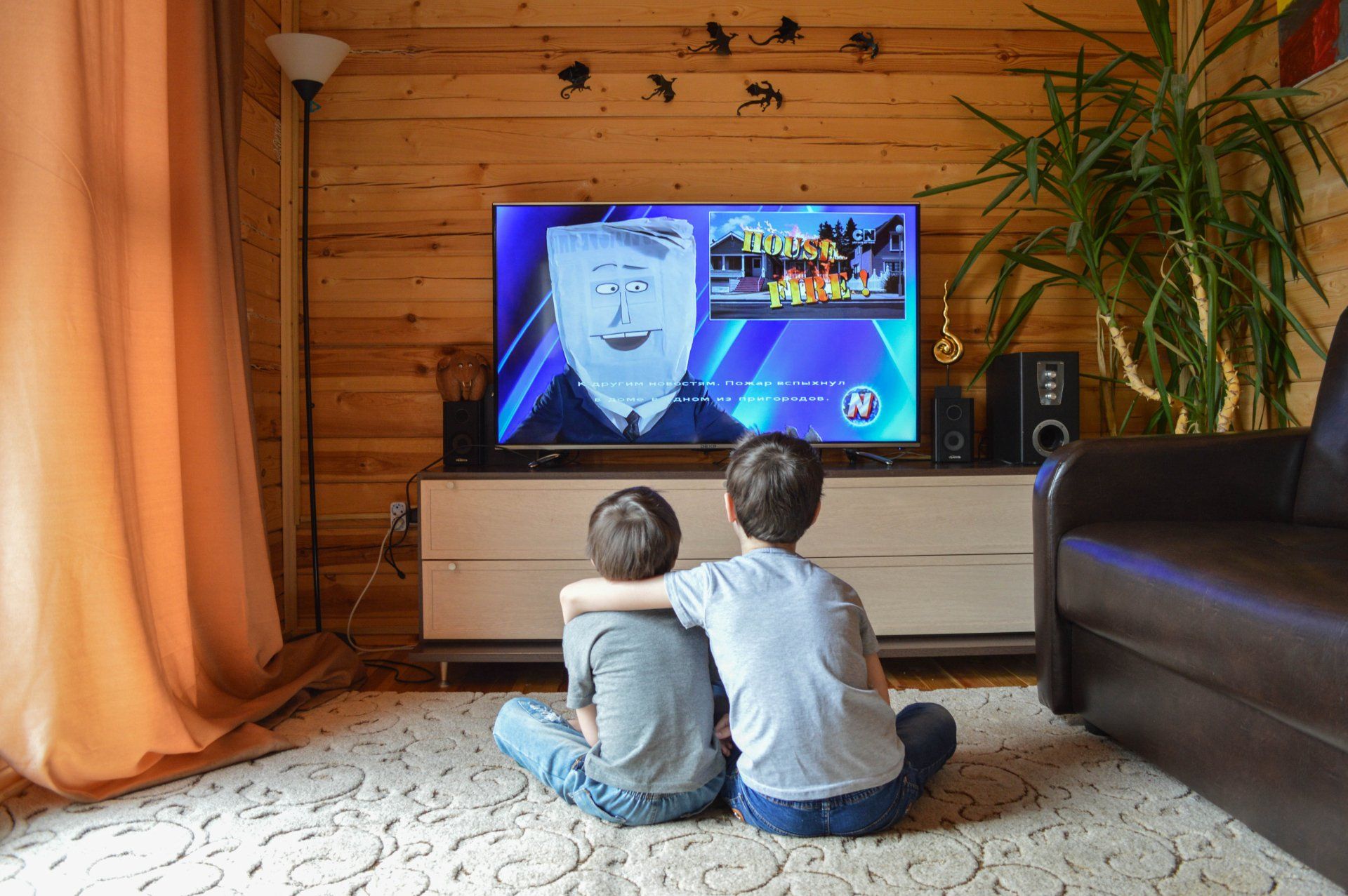 Two boys are sitting on the floor watching a television.