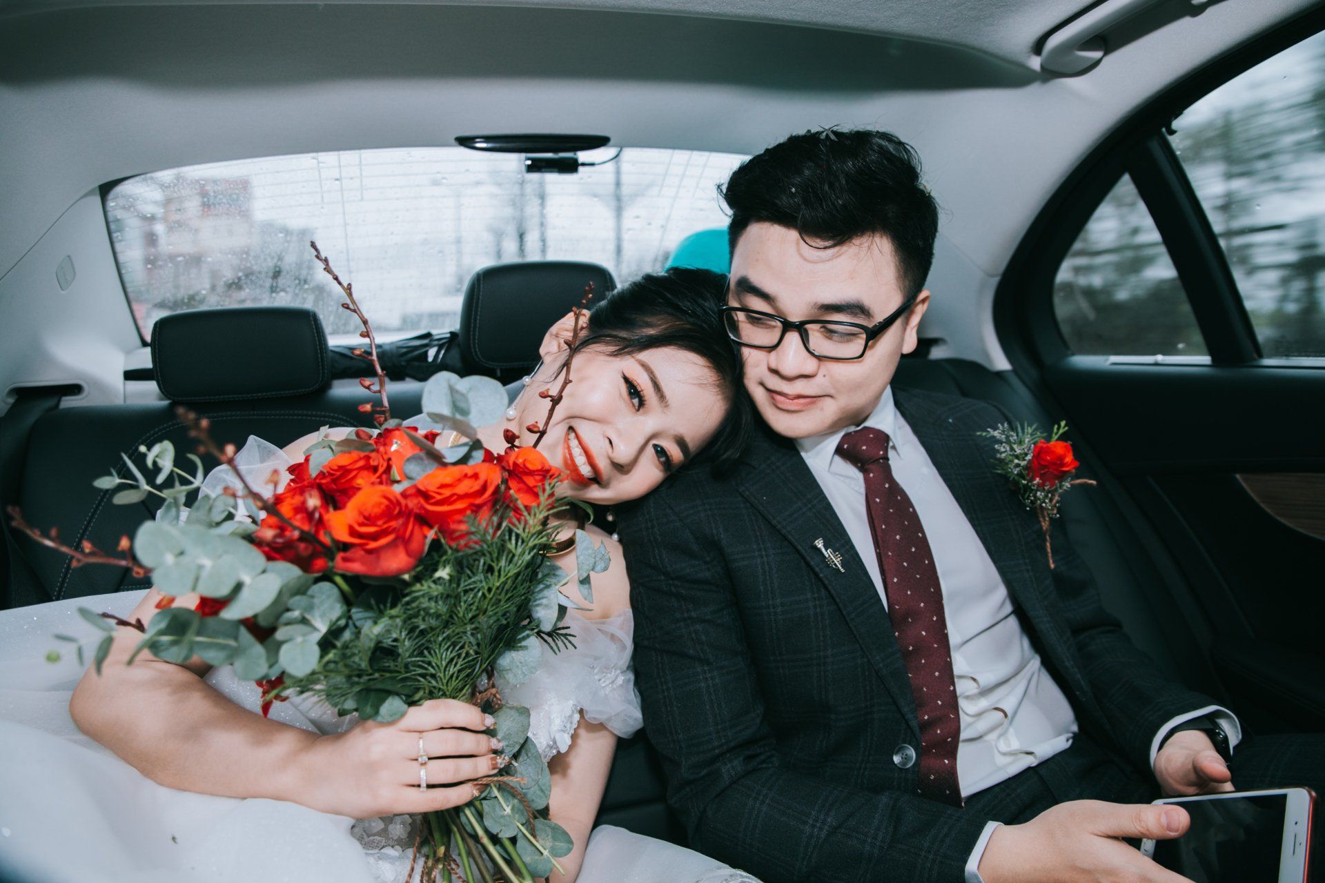 A bride and groom are sitting in the back seat of a car.