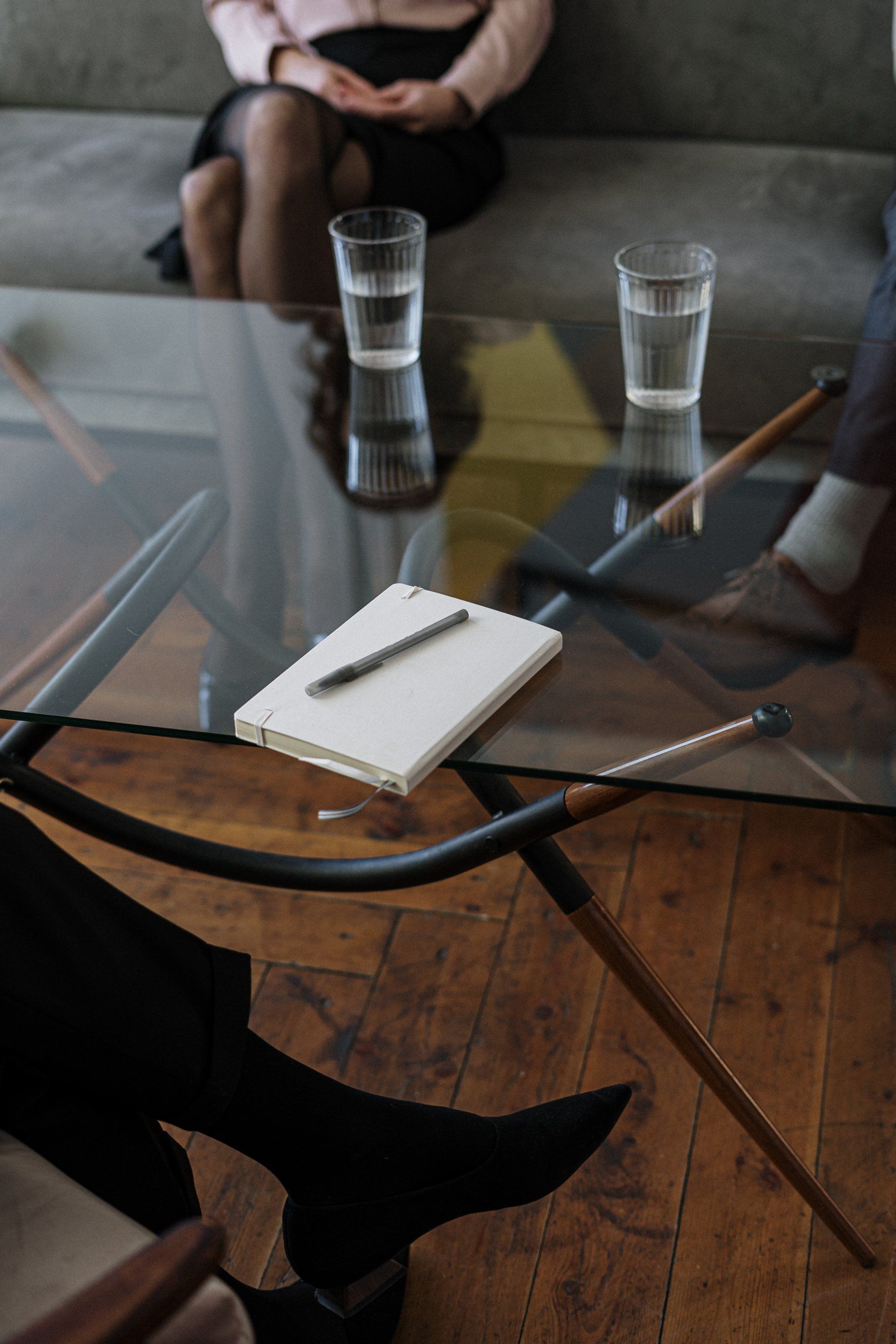 A notebook sitting on top of a clear glass table accompanied by two cups of water and a pen.
