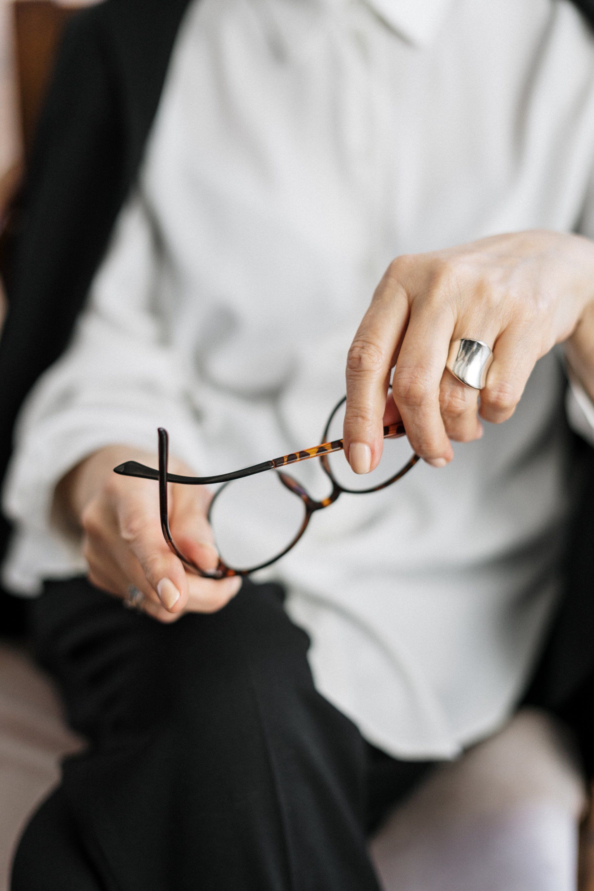 A woman wearing a ring is holding a pair of glasses.