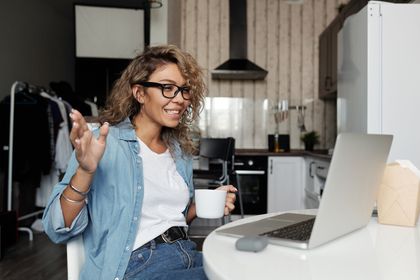 A woman is sitting at a table with a laptop and a cup of coffee.