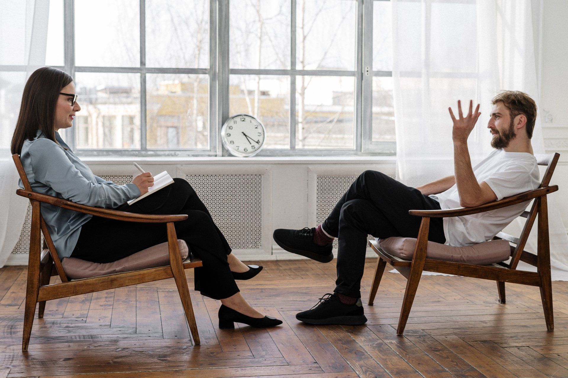 A man and a woman are sitting in chairs talking to each other.
