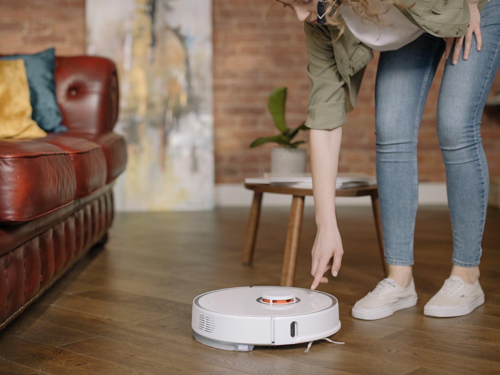 A woman is pointing at a robot vacuum cleaner in a living room.