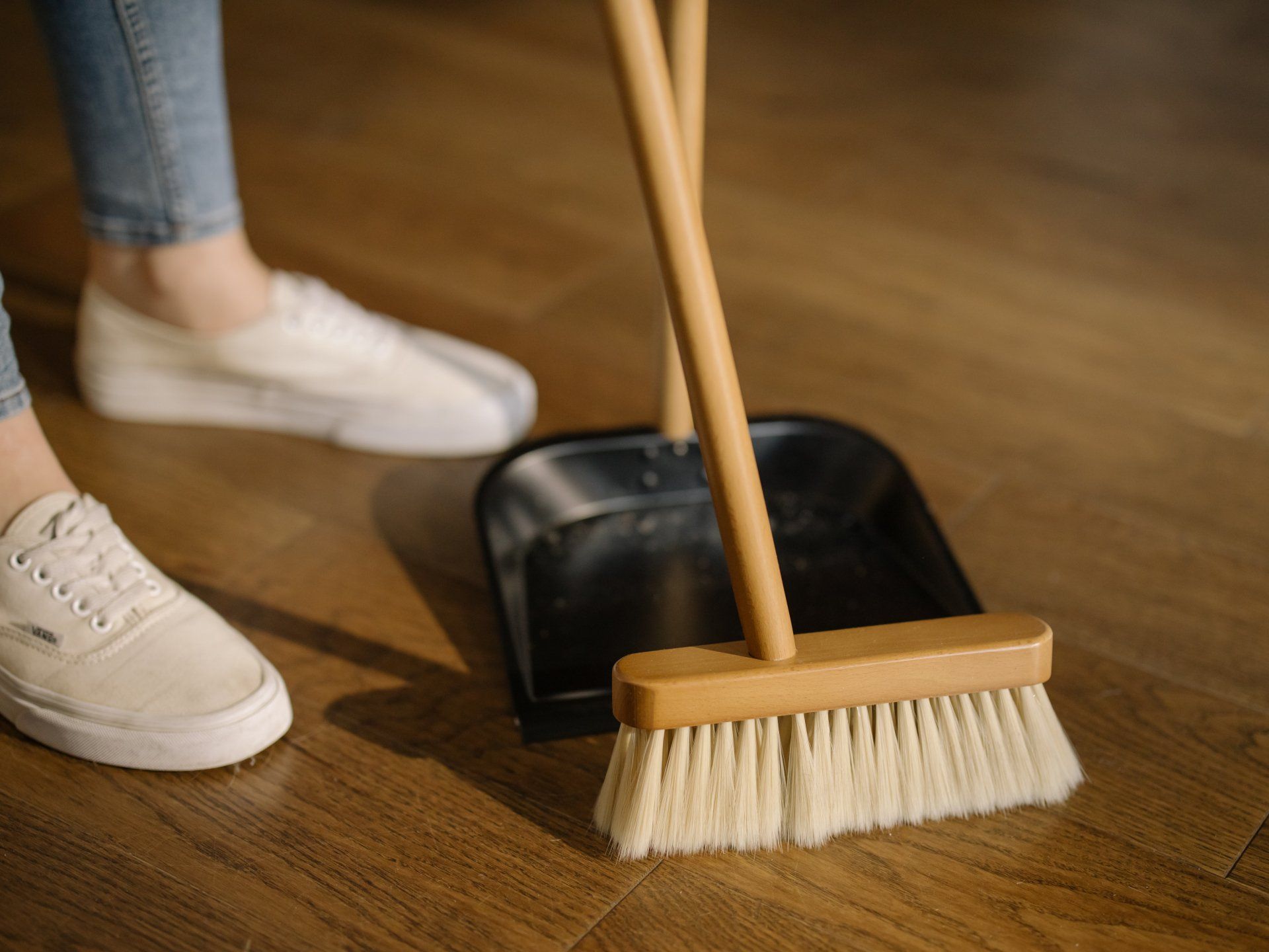 Cleaner sweeping the floor with a broom and collecting debris into a dustpan.