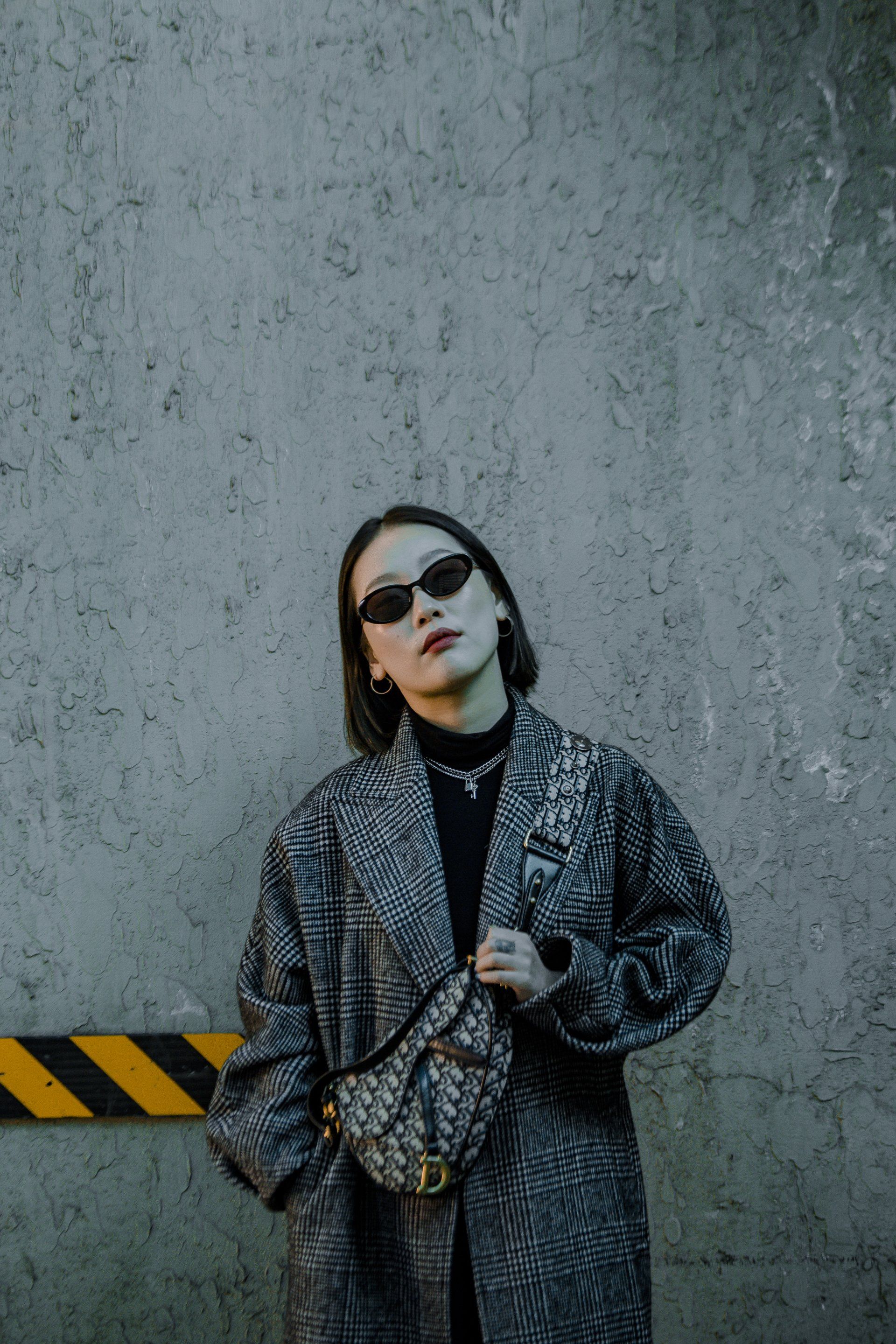 A woman standing up against a slate grey concrete wall