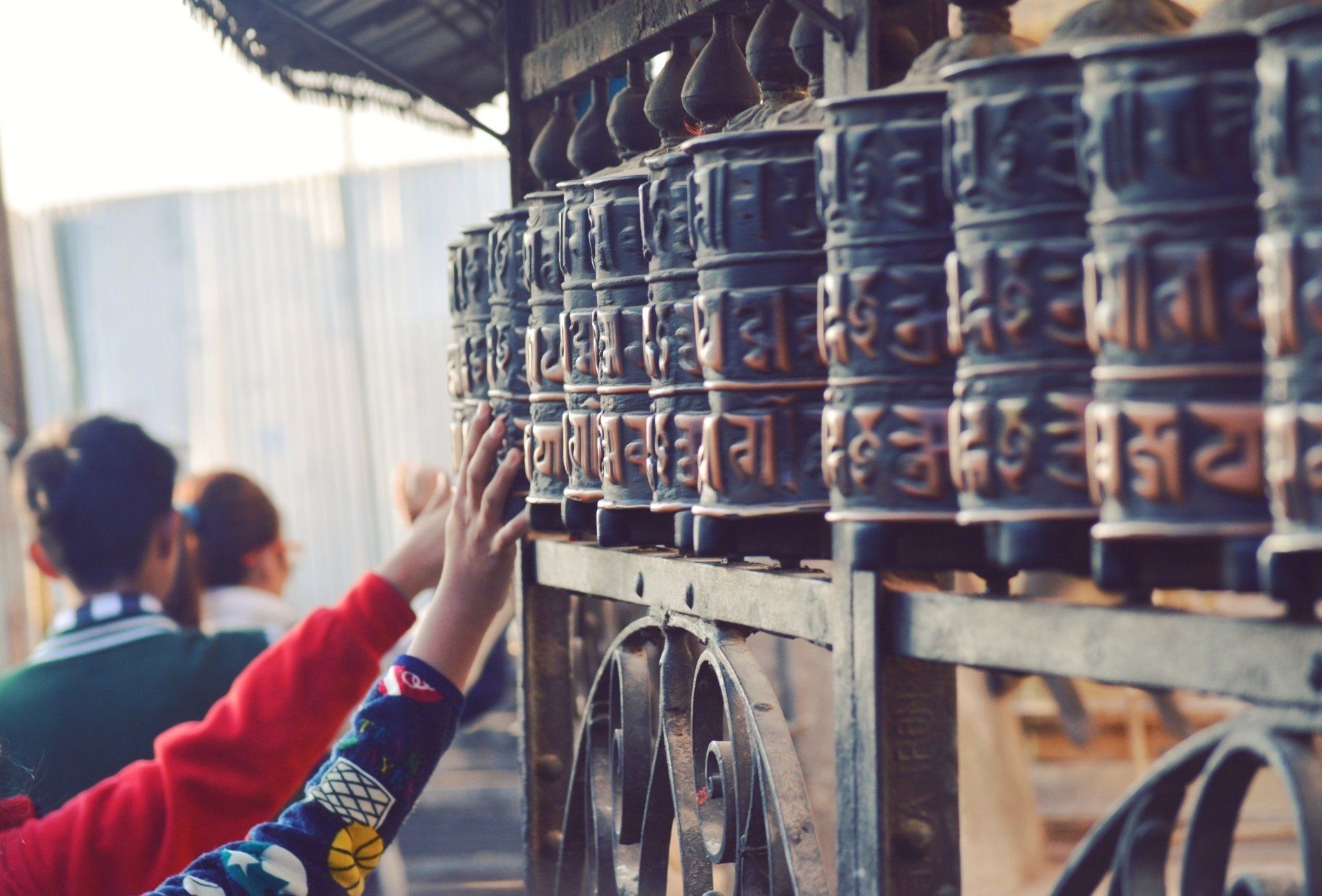 A person is praying in front of a row of prayer wheels.