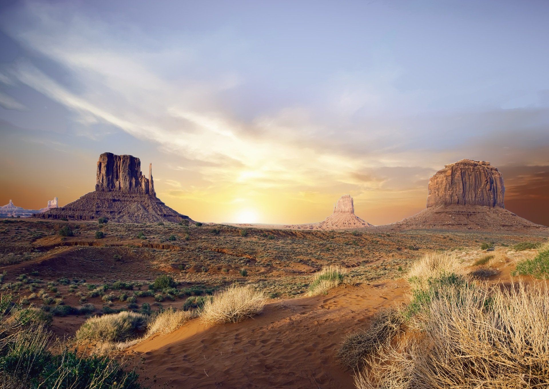 The sun is setting over a desert landscape with mountains in the background.