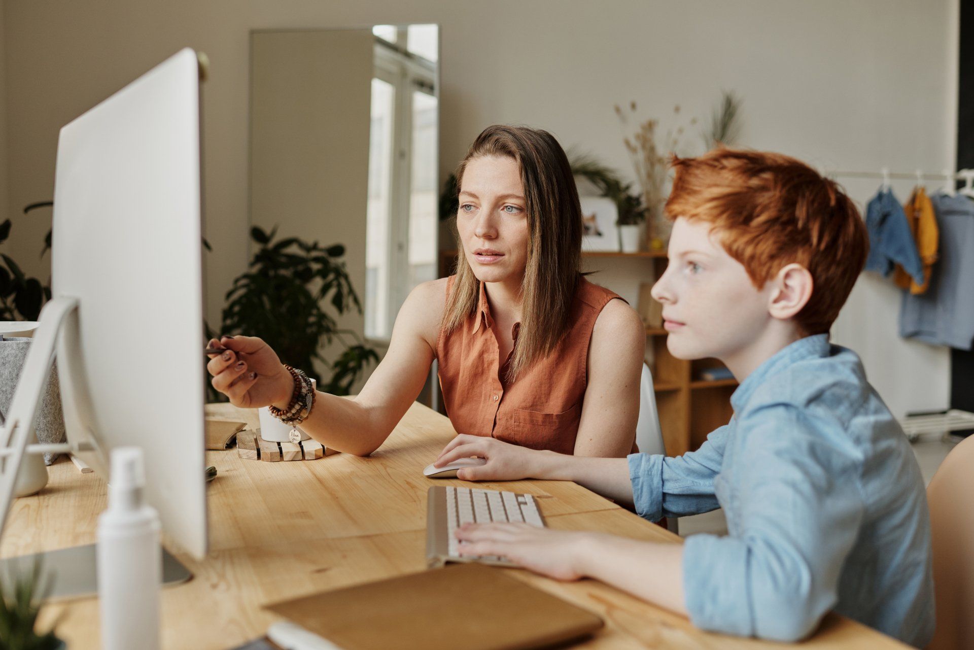 A mother and teenage son sat together at a desktop computer.