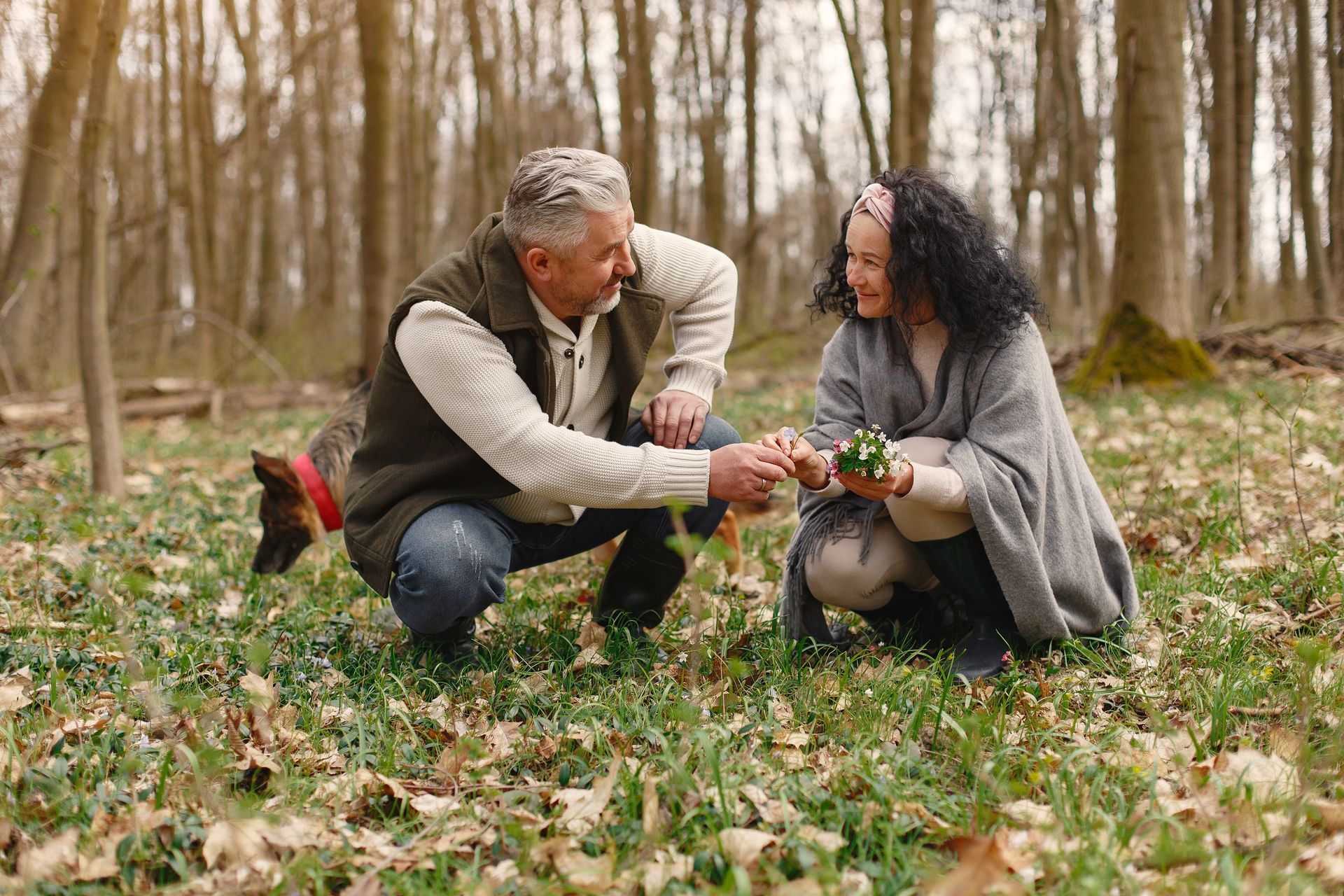 A man and a woman are kneeling in the grass in the woods.