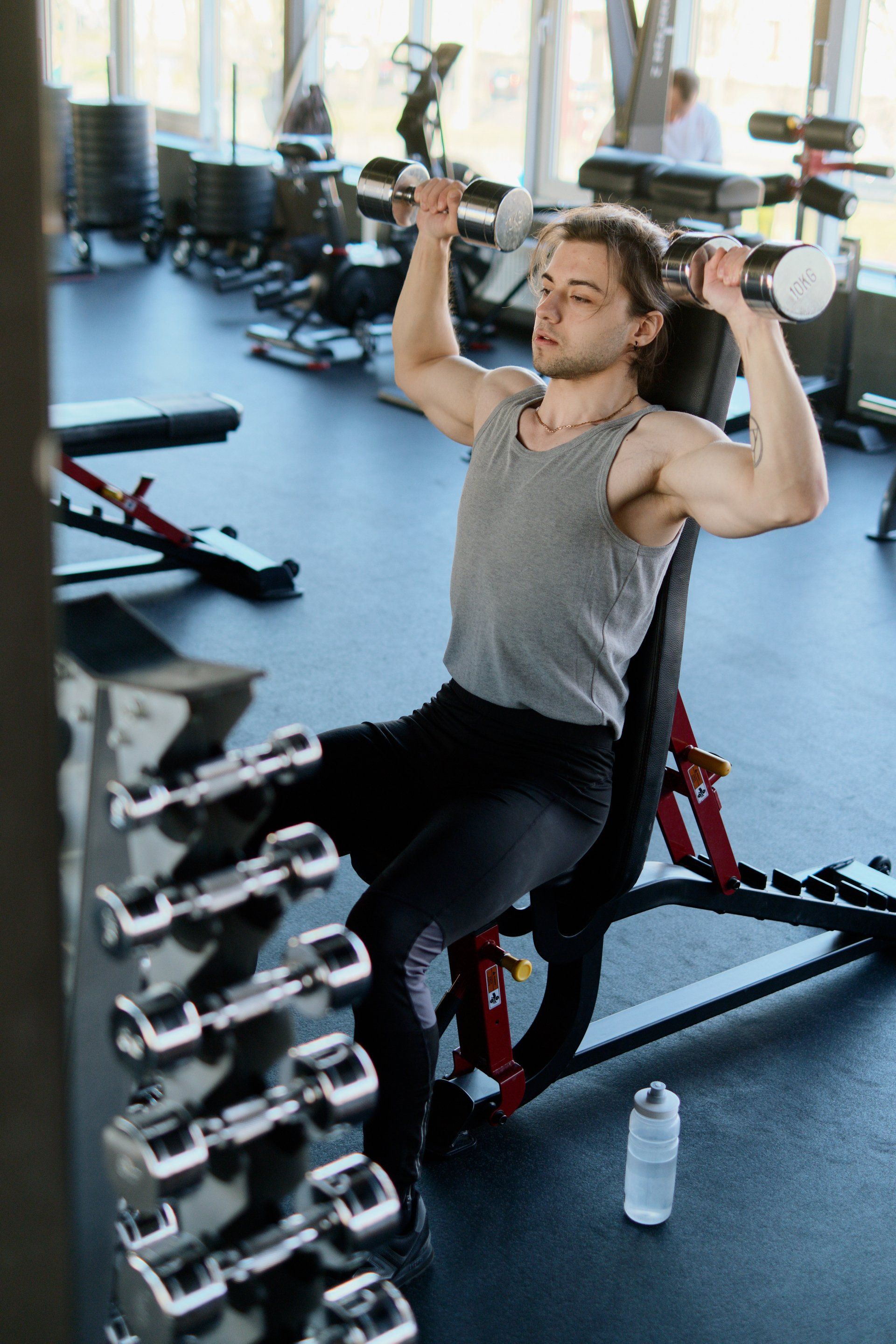 a man is sitting on a bench in a gym lifting dumbbells .