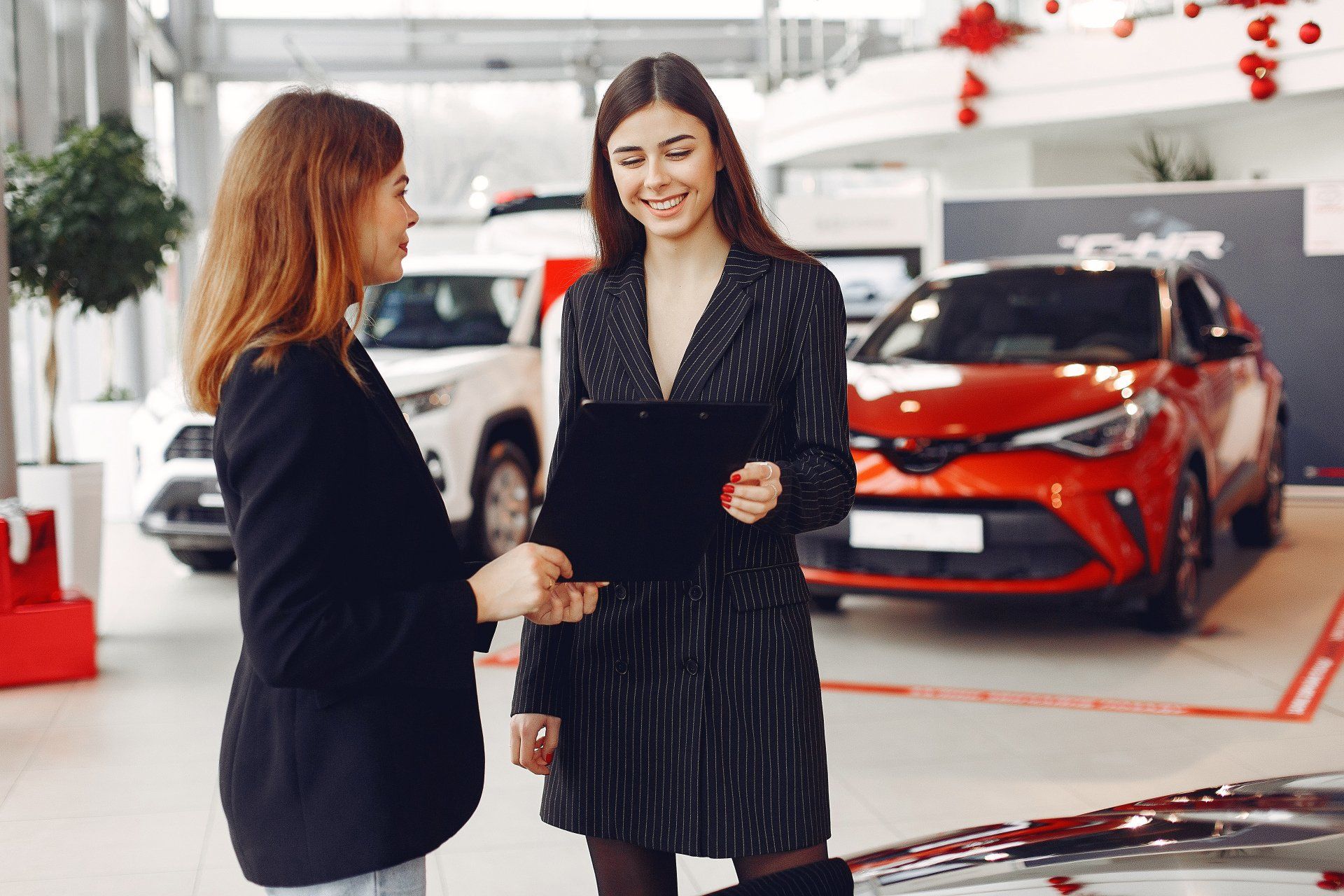 Two women are standing next to each other in a car showroom.