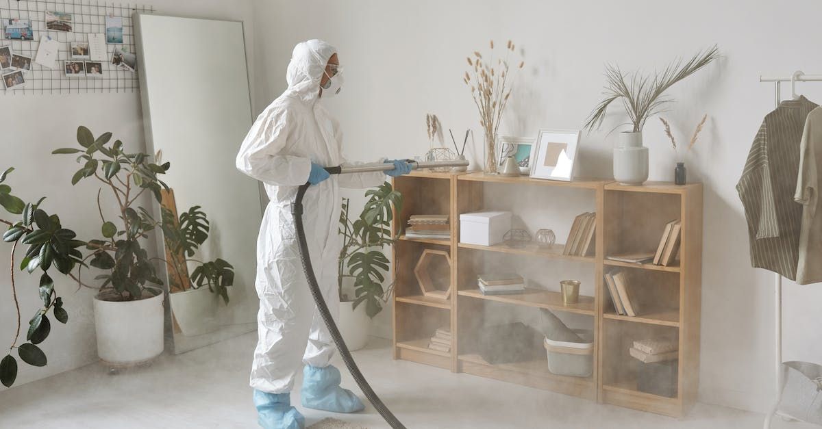 A person in a protective suit is cleaning a room with a vacuum cleaner.