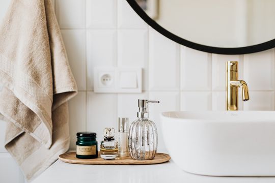 A bathroom with a sink , mirror , towel and bottles of perfume.