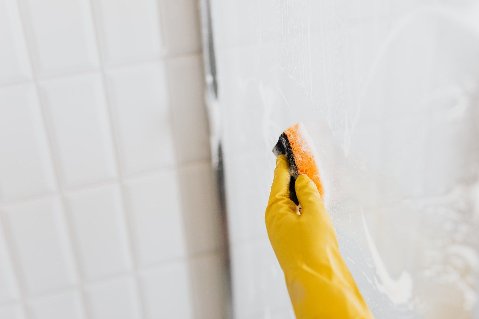 Person cleaning a glass partition in a bathroom using a sponge.