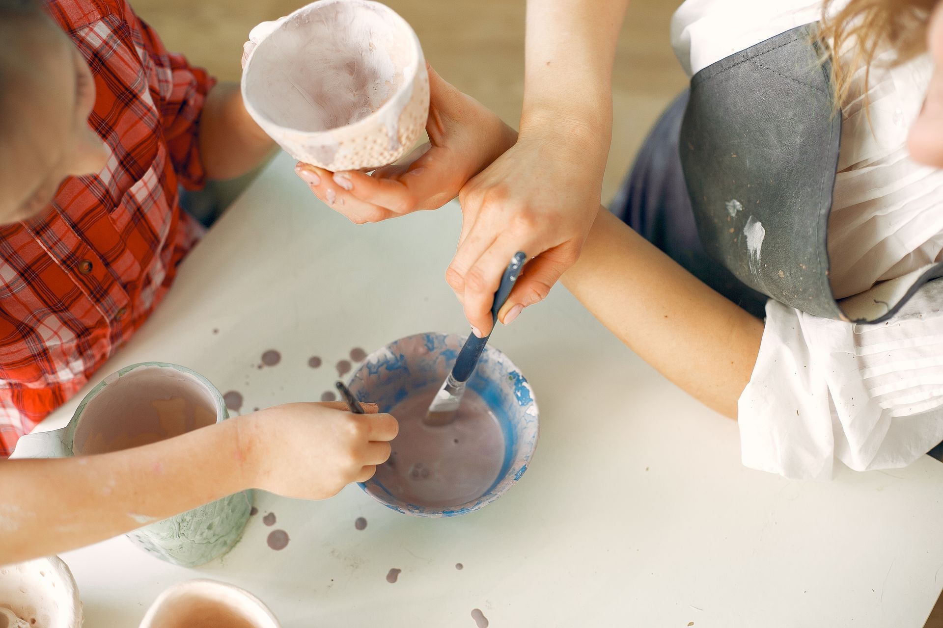 A woman and two children are sitting at a table making clay pots.