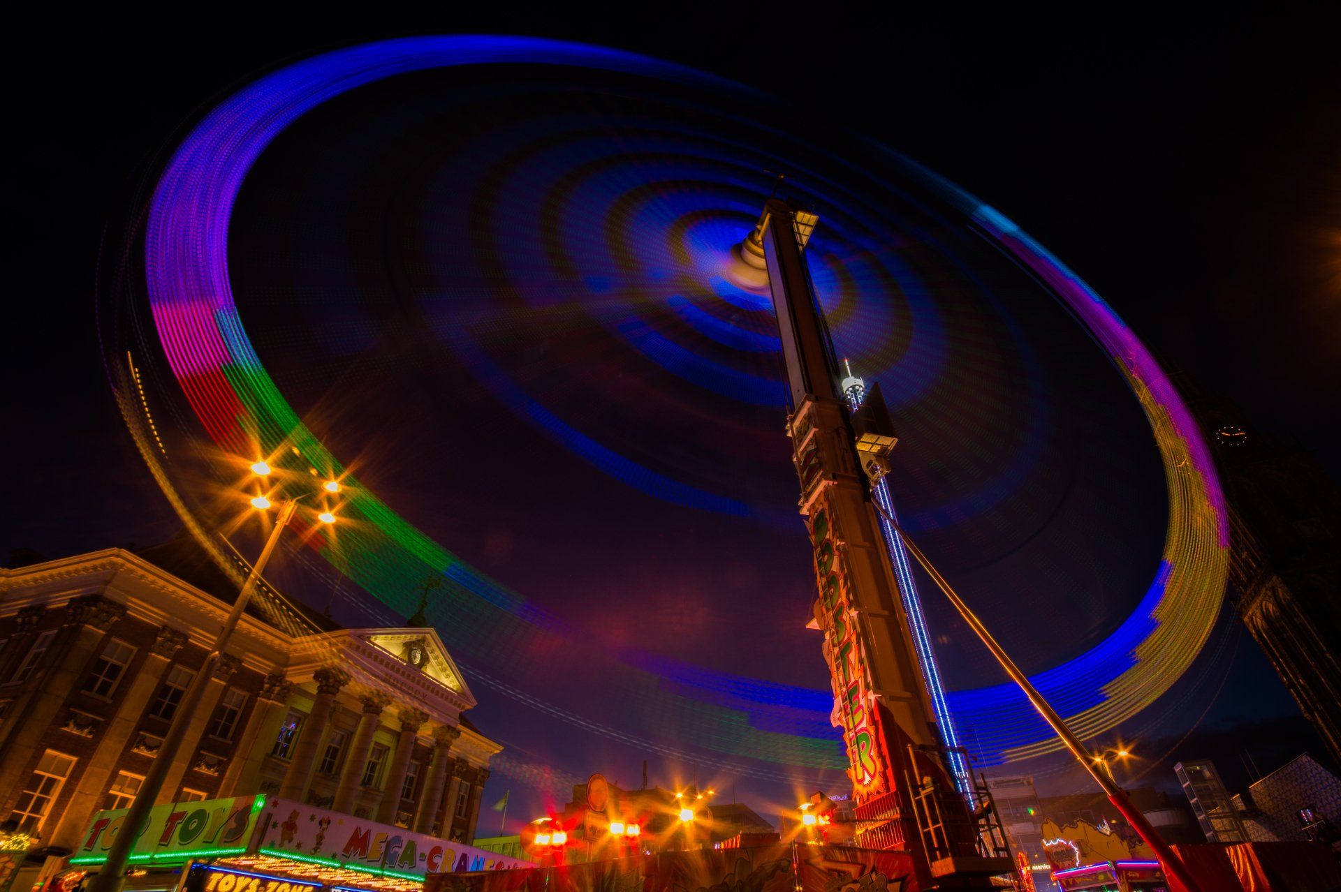 a colorful ferris wheel is spinning in the dark showcasing the light effect from slower shutter speeds