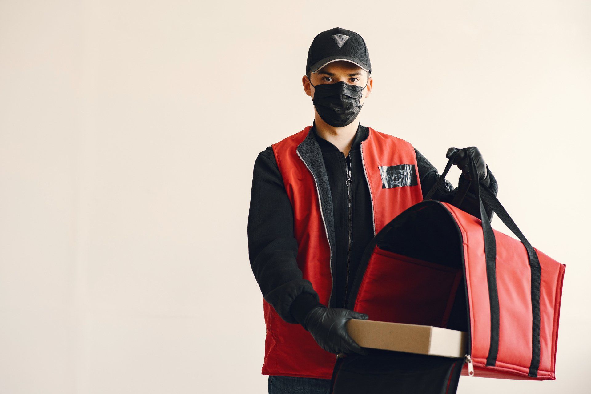 a delivery man wearing a mask and gloves is holding a bag and a box .