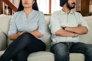 A man and a woman are sitting on a couch with their arms crossed.