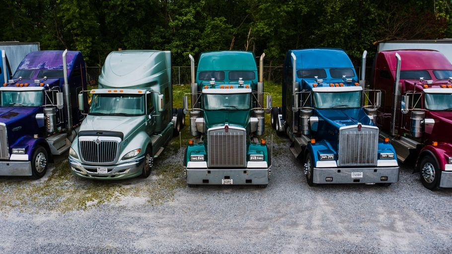 A row of semi trucks are parked in a gravel lot.