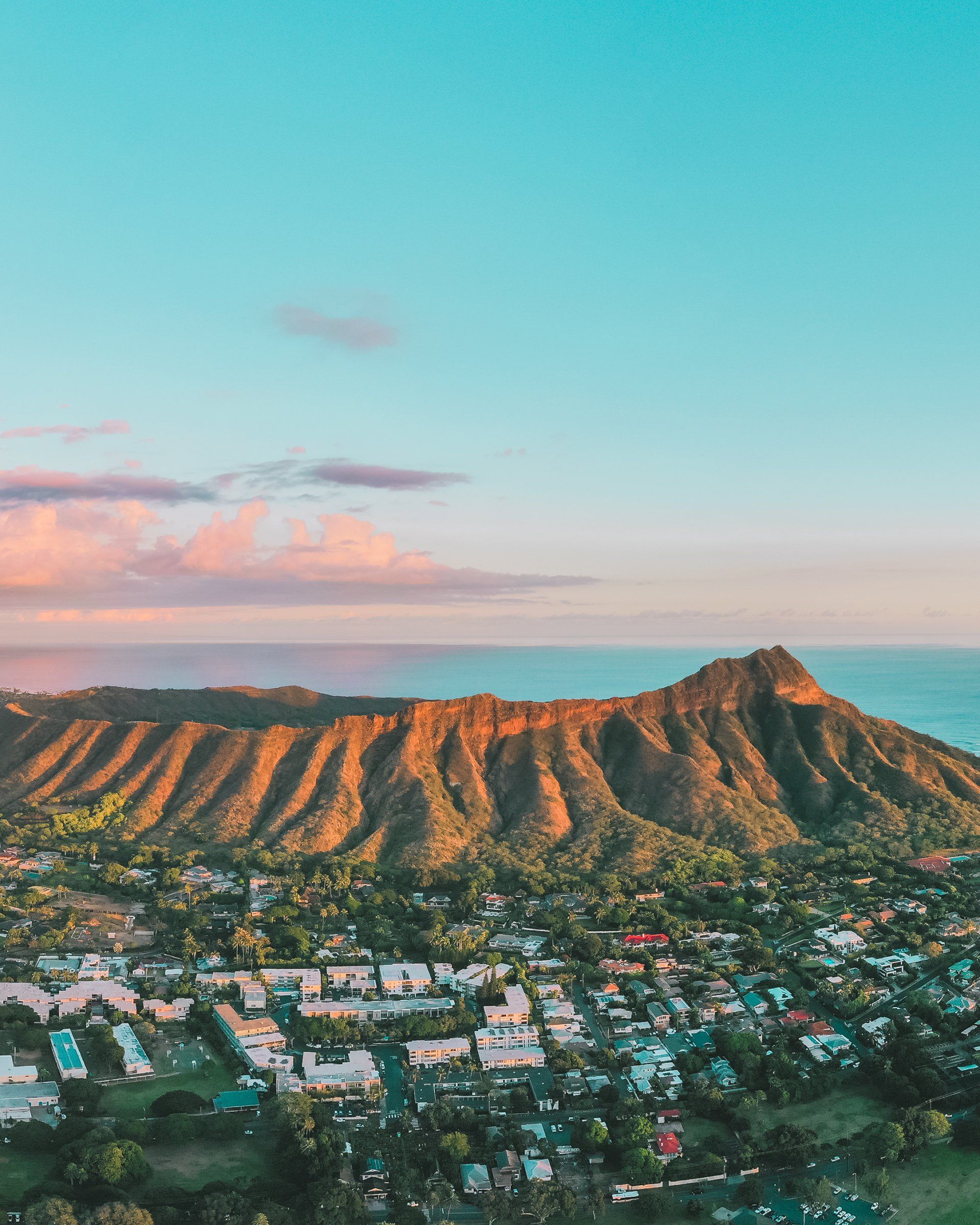 An aerial view of a mountain with a city in the foreground and the ocean in the background.
