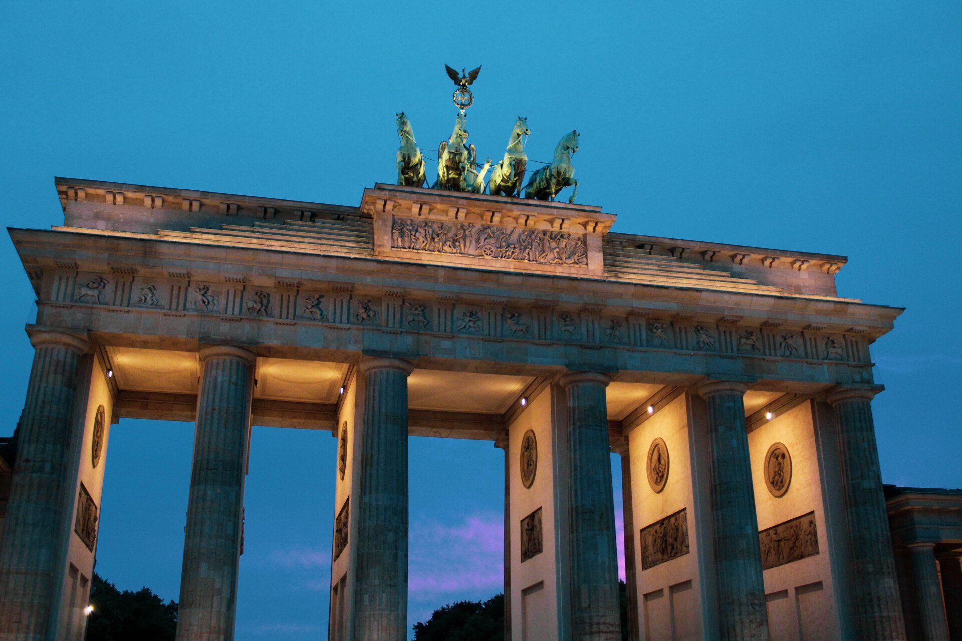 Das Berliner Brandenburger Tor ist nachts beleuchtet, im Hintergrund ein blauer Himmel