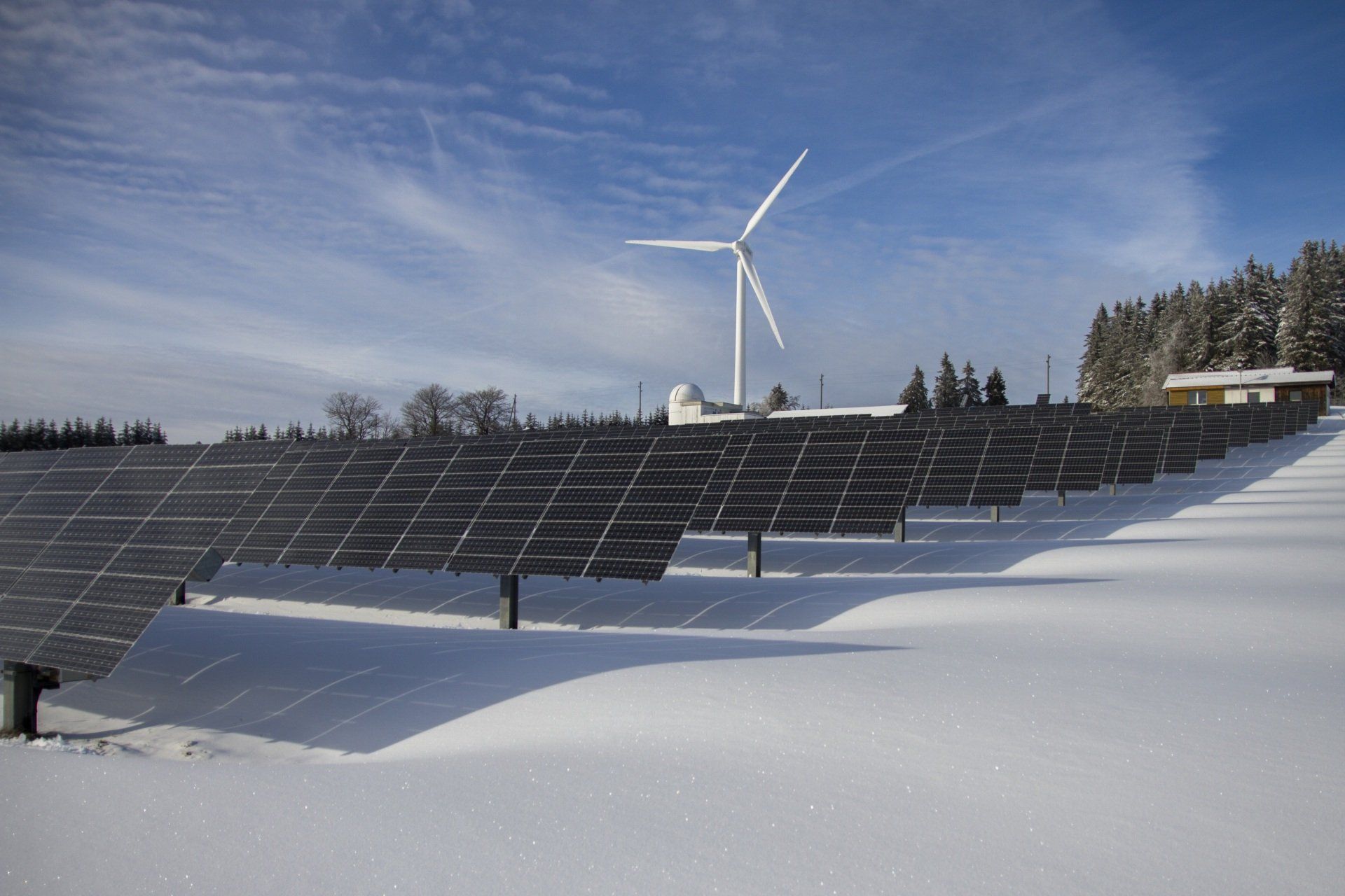 a row of solar panels in the snow with a wind turbine in the background .