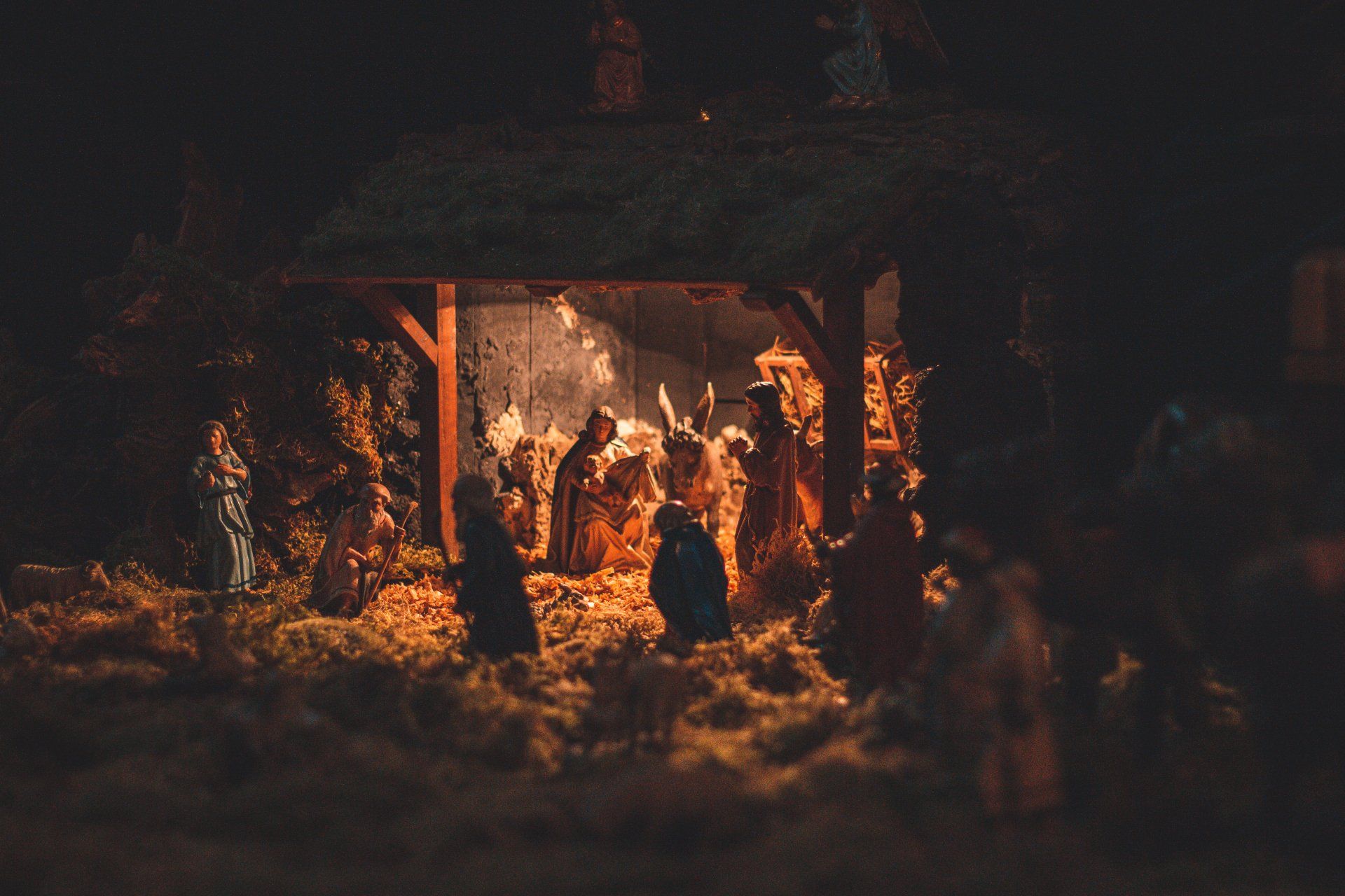 A nativity scene with sheep and people in a stable at night.