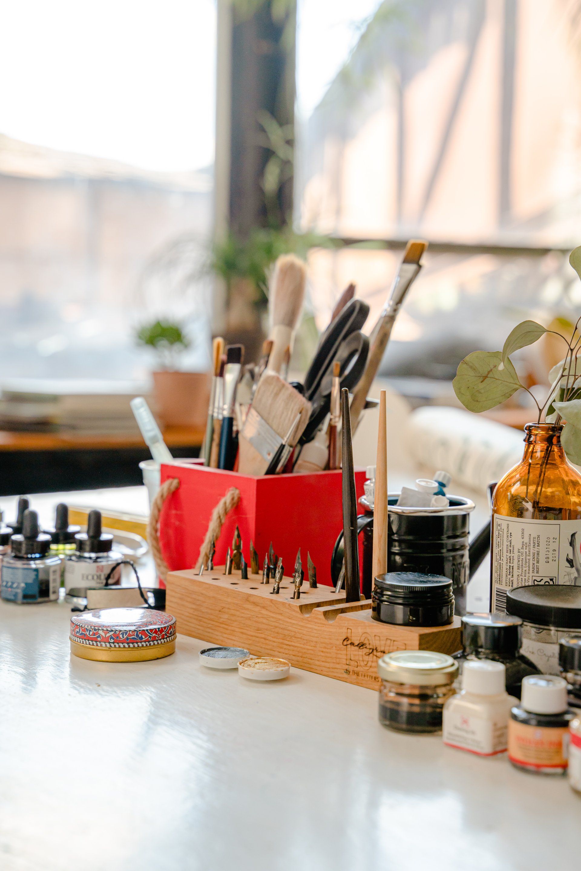 A table with a red box filled with brushes and bottles of paint.