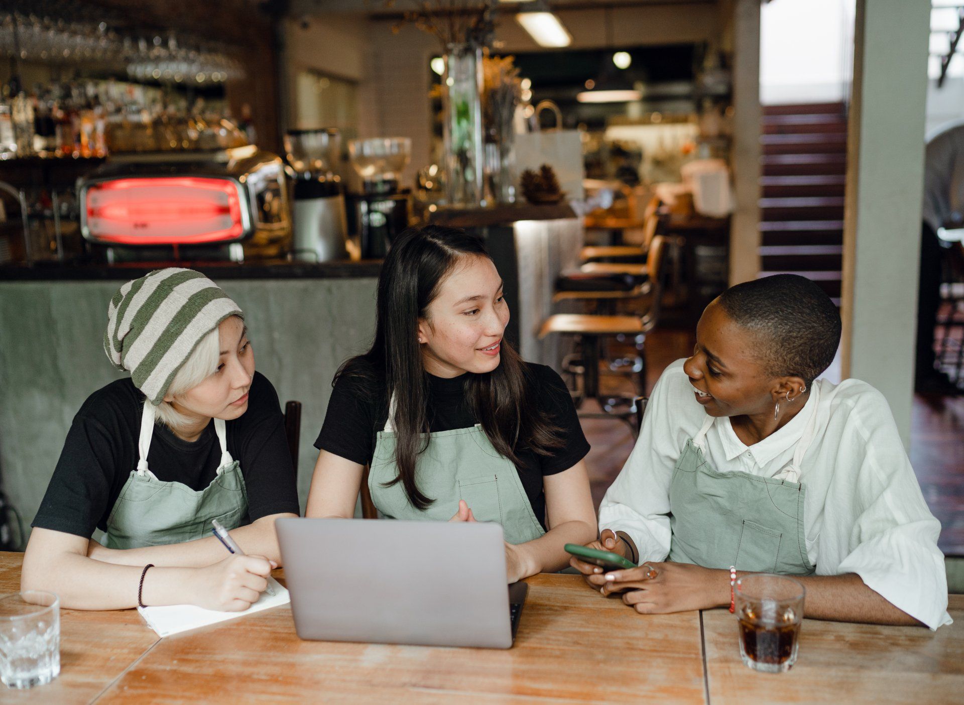 three women are sitting at a table in a restaurant looking at a laptop .