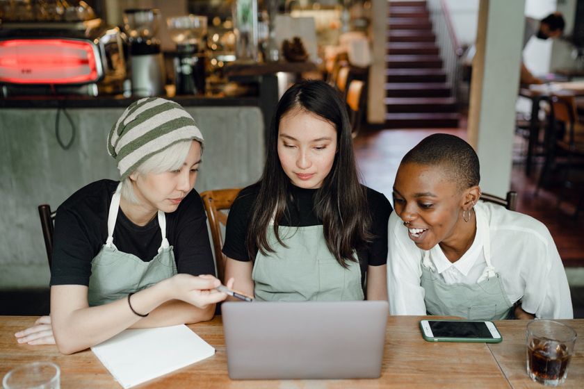 Three women are sitting at a table looking at a laptop computer.