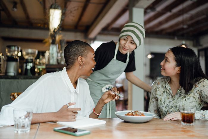 A waitress is serving food to two women at a table in a restaurant.