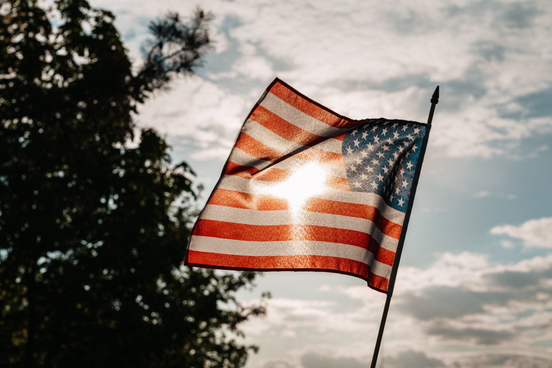 An american flag is waving in the wind with the sun shining through it.