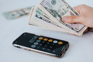 A person is holding a bunch of money next to a calculator.