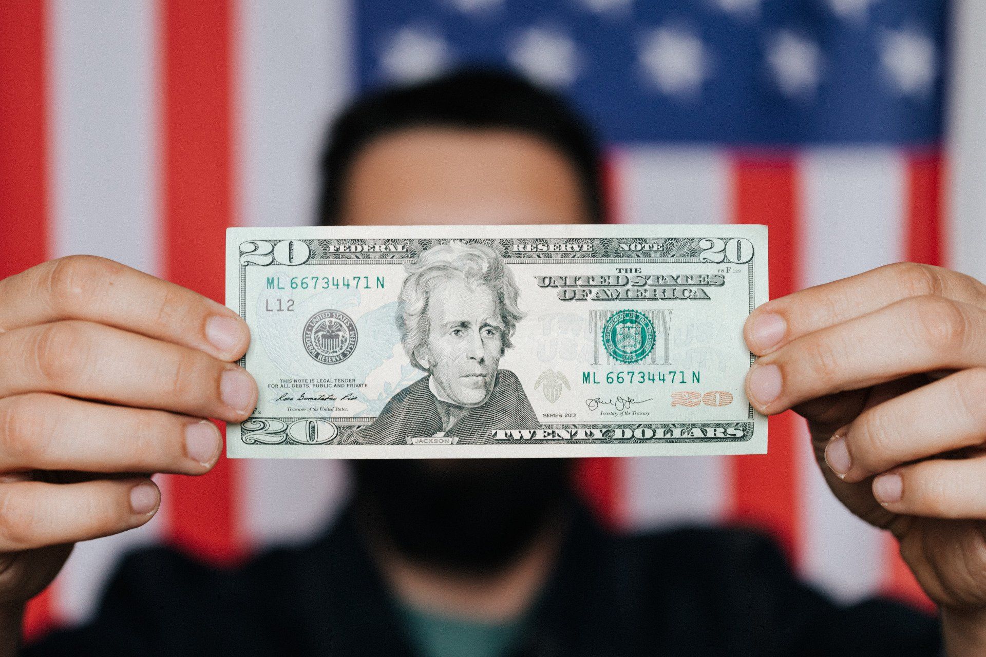 A man is holding a 20 dollar bill in front of an american flag.