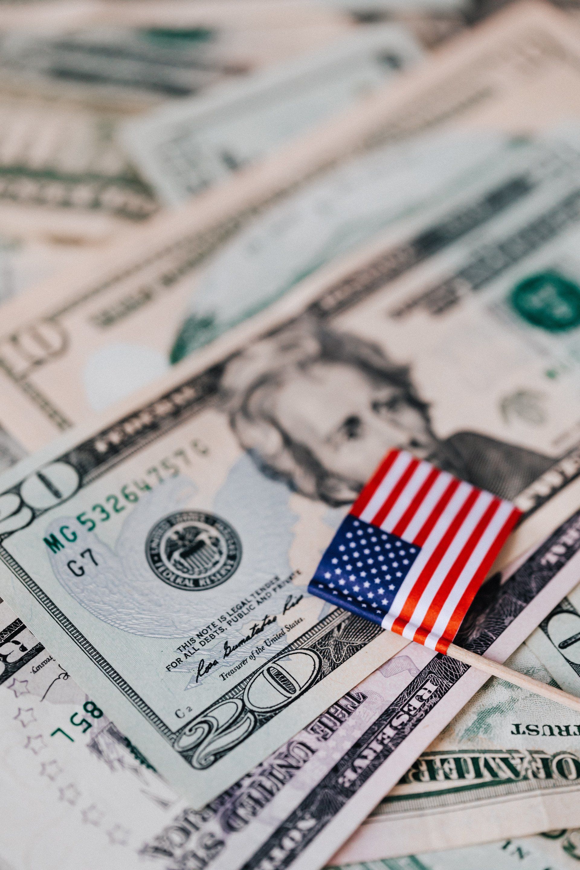 Several U.S Dollars of varying amounts sitting in a pile with a tiny U.S flag on top