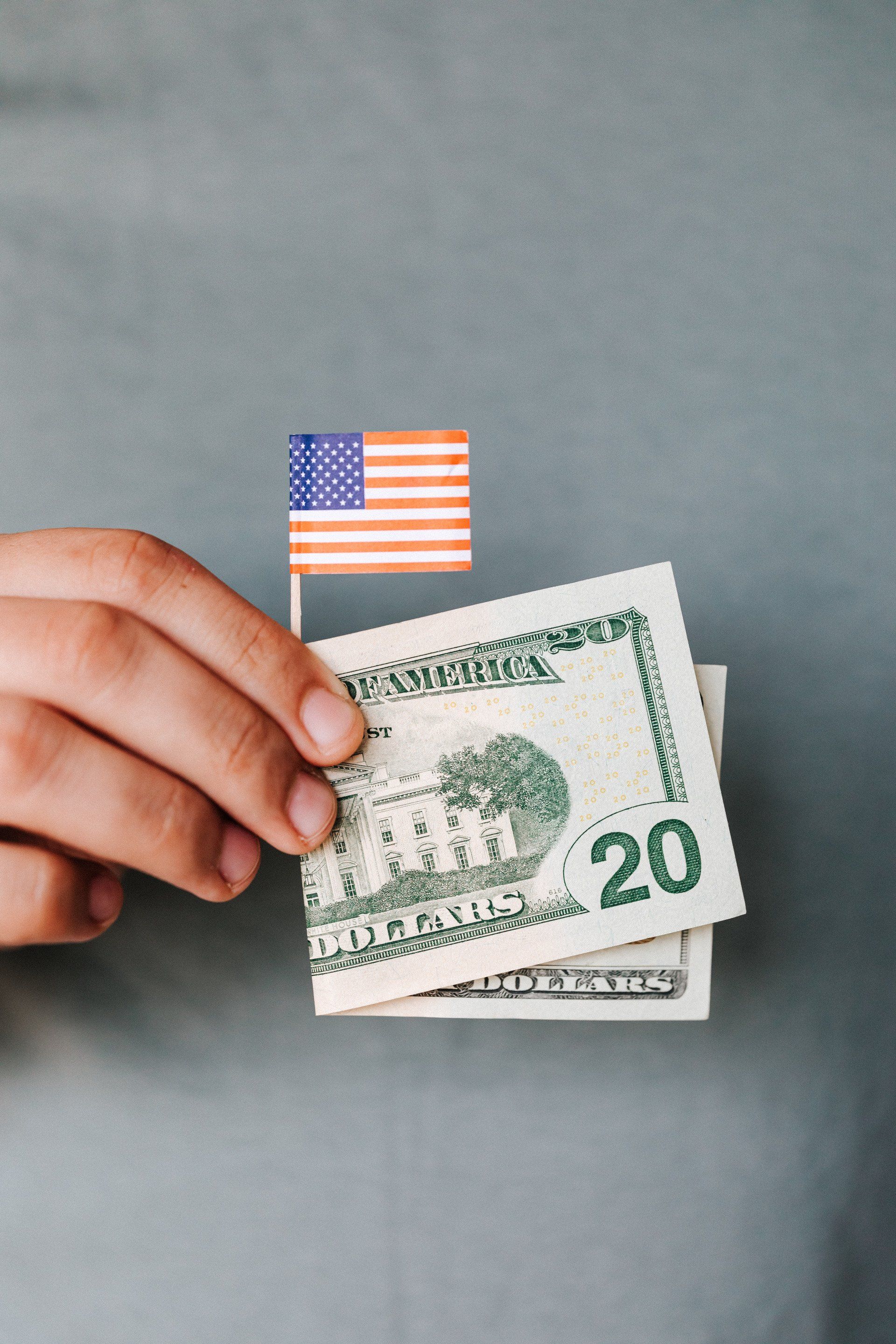 A person is holding a 20 dollar bill with an american flag sticking out of it.