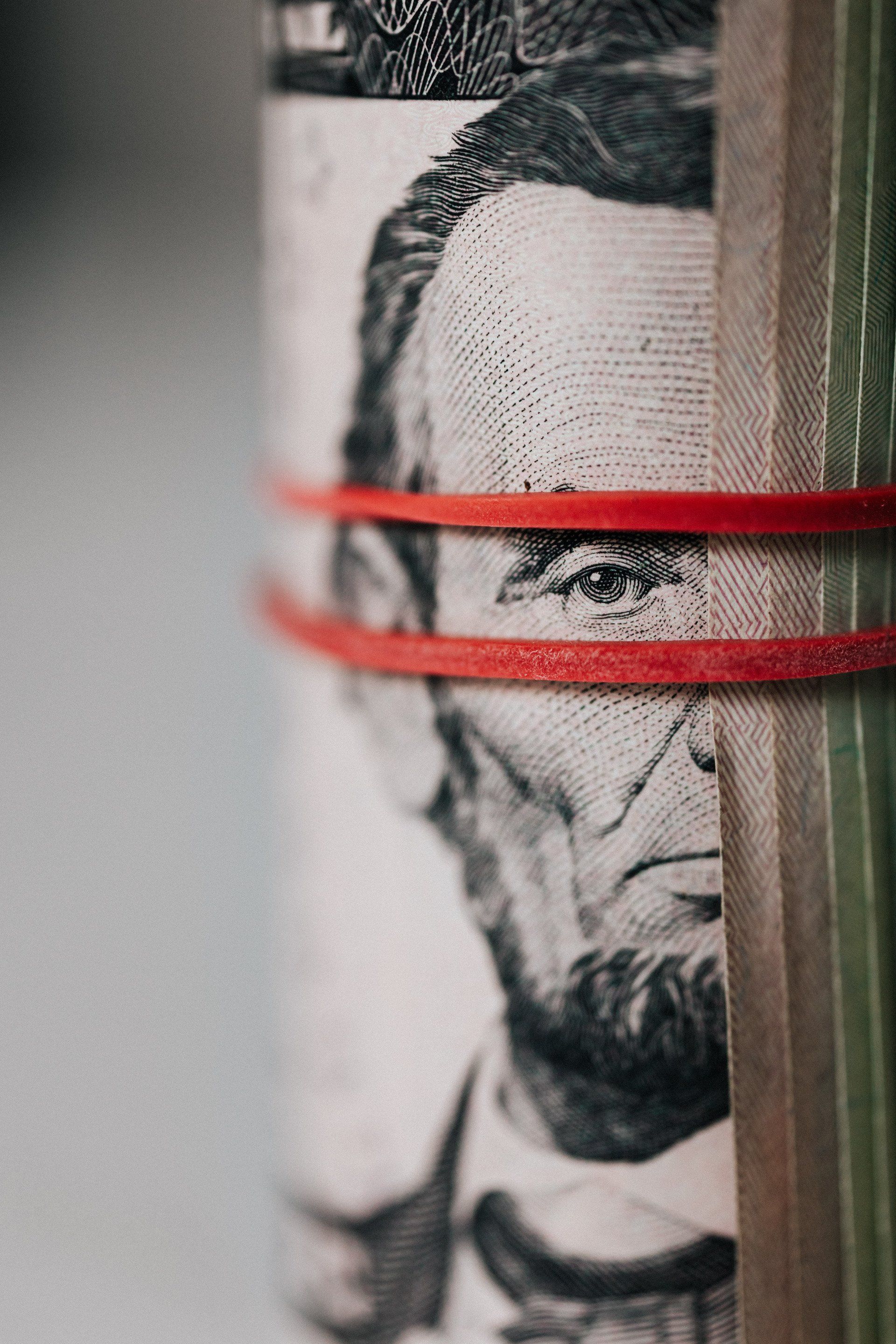 A close up of a roll of money with a red rubber band around it.